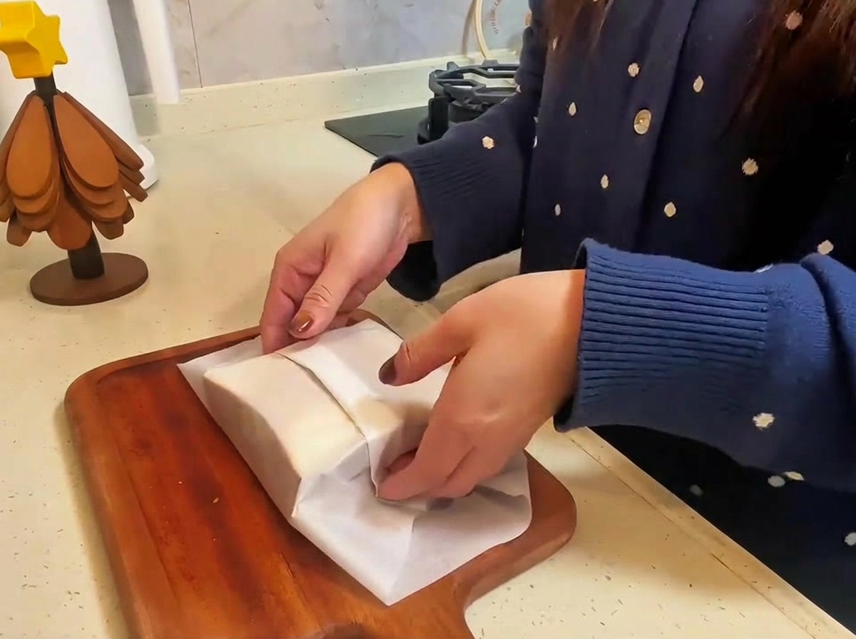 Gotowa kanapka z wołowiną i serem zawinięta w papier do pieczenia i przekrawana na pół na drewnianej desce.