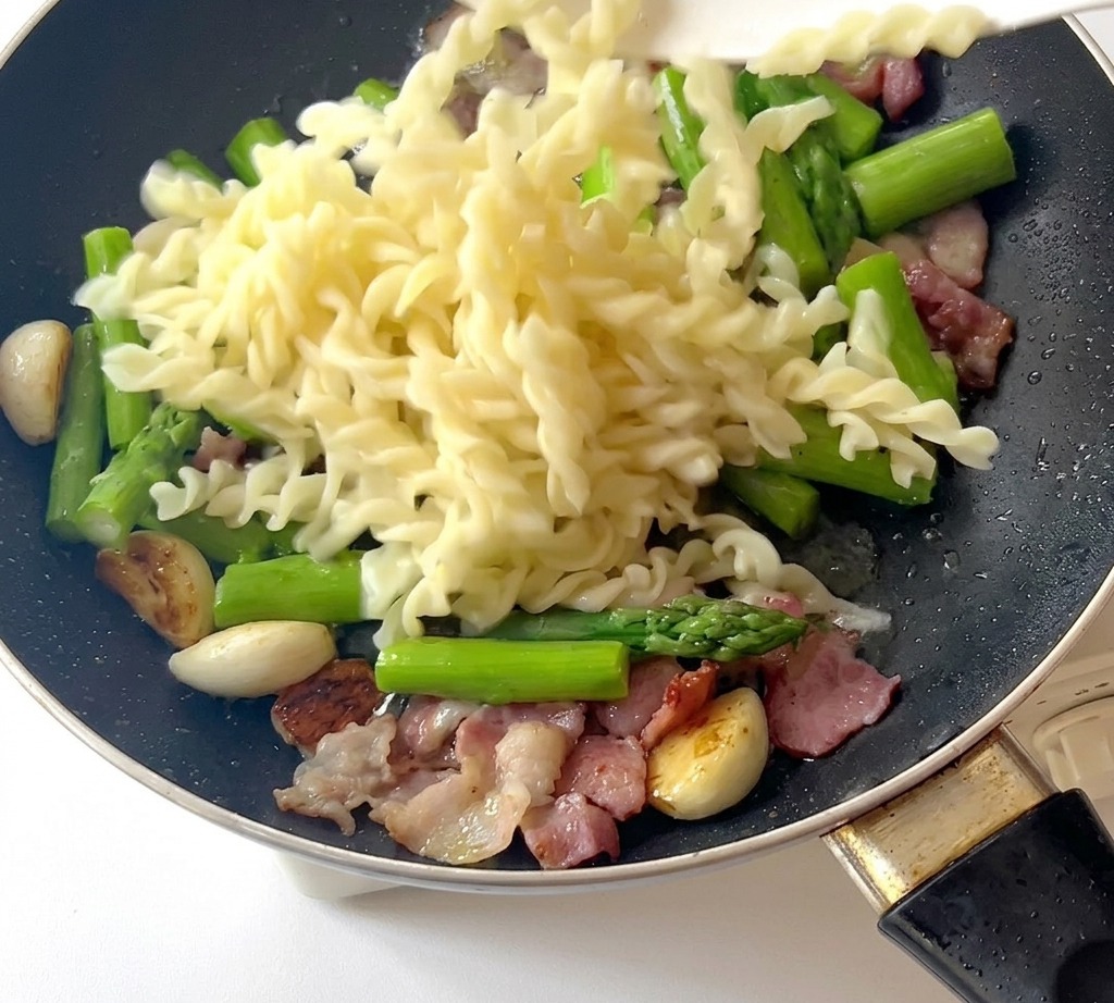 Ugotowany makaron fusilli dodawany do patelni ze składnikami.