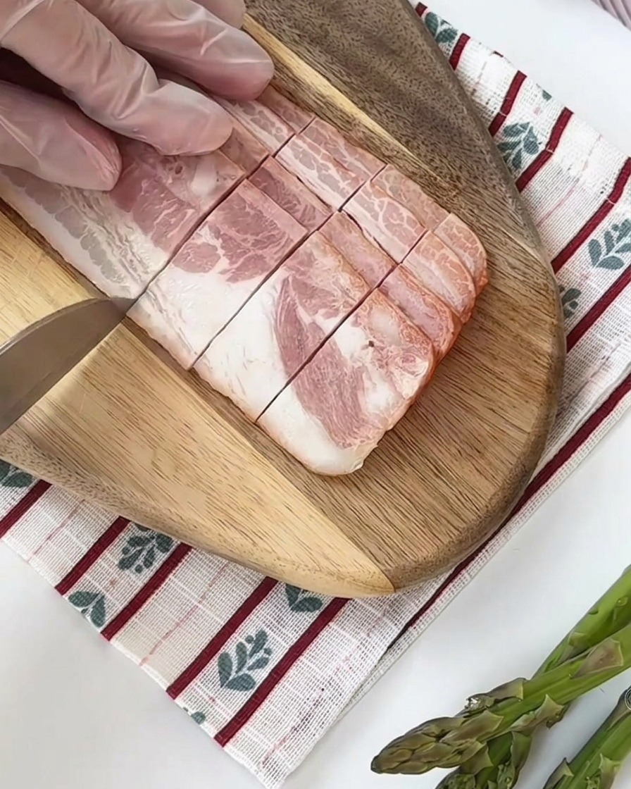 Świeże zielone szparagi krojone na równe kawałki na desce do krojenia.