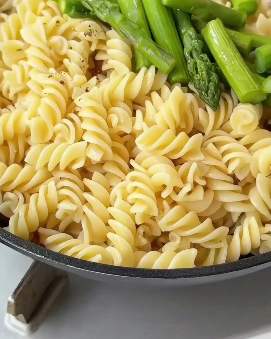 Fusilli i zielone szparagi na patelni przyprawiane świeżo mielonym pieprzem.