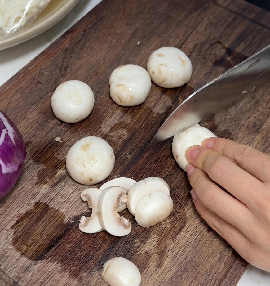Świeże pieczarki krojone w cienkie, równe plasterki na desce do krojenia.