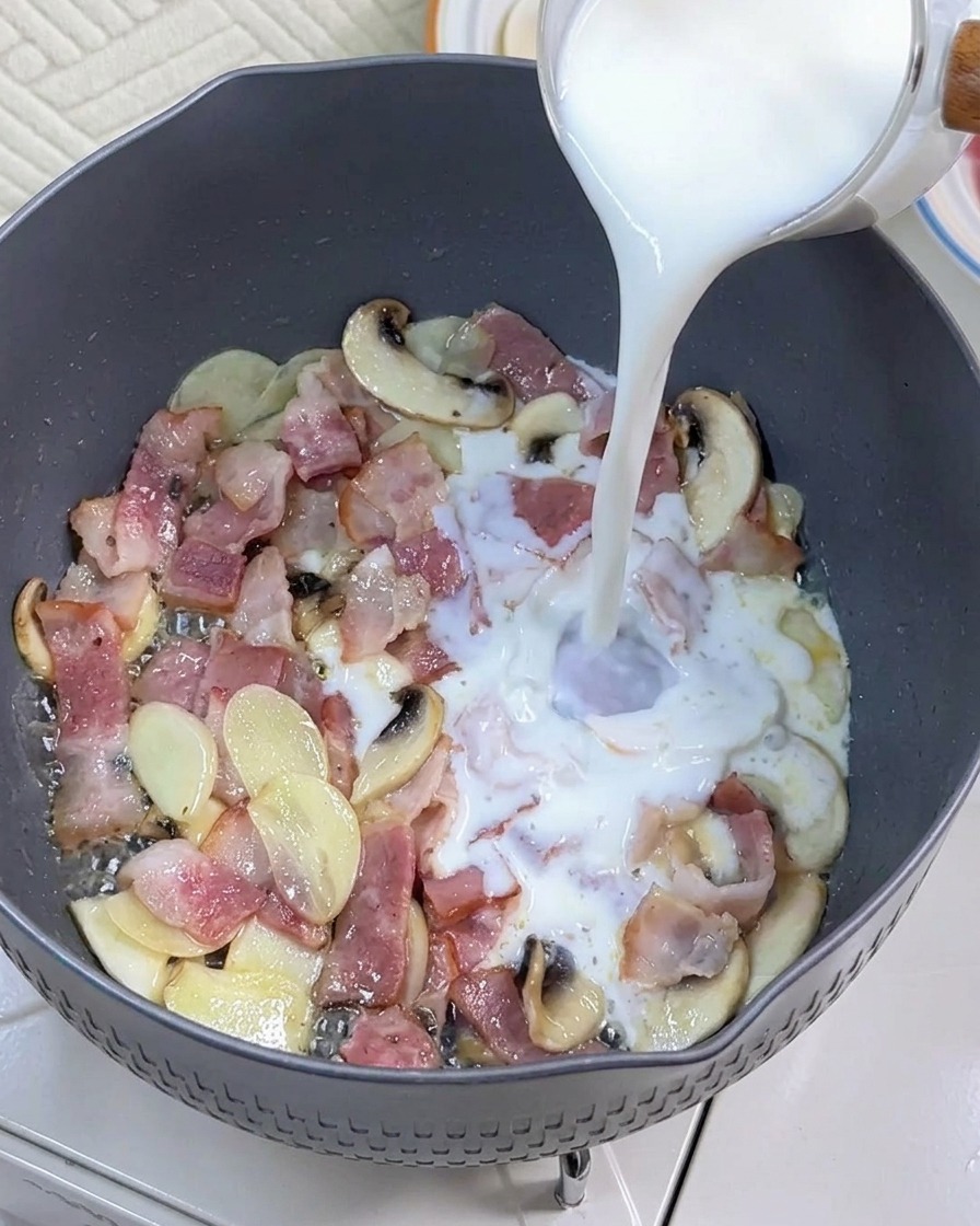Mleko wlewane na patelnię z usmażonym boczkiem i pieczarkami.