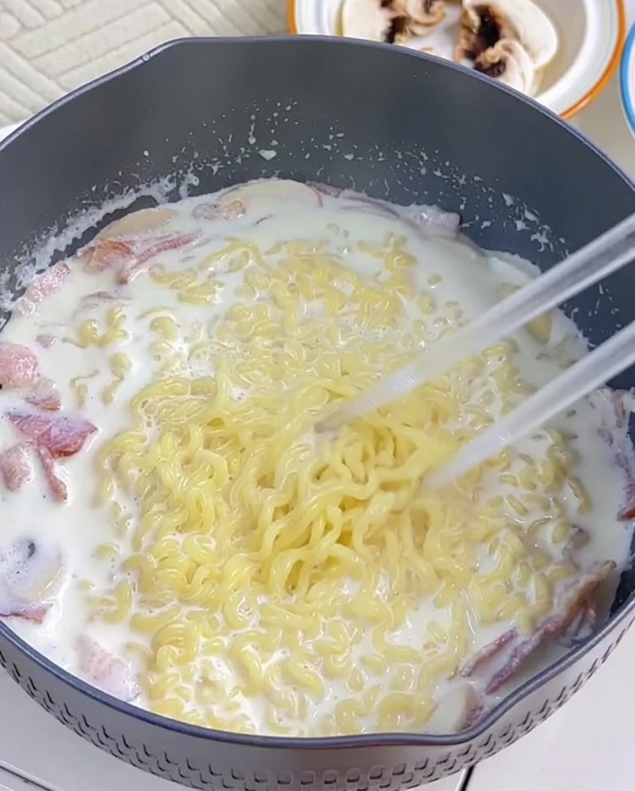 Makaron ramen mieszany z kremowym sosem za pomocą pałeczek.