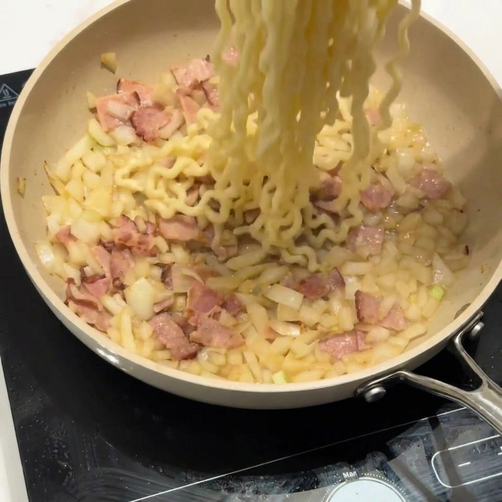Makaron typu curly dodawany do patelni z boczkiem i cebulą.