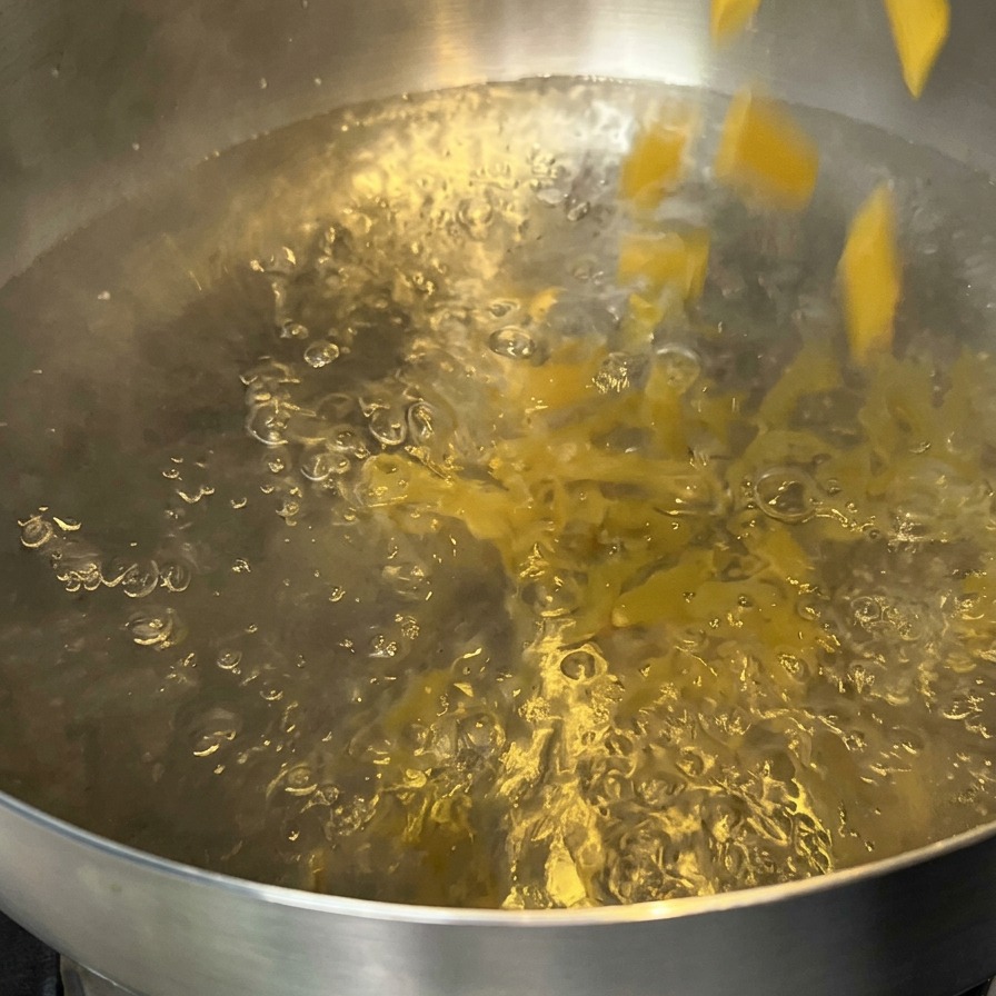 Surowy makaron penne wsypywany do garnka z wrzącą wodą.