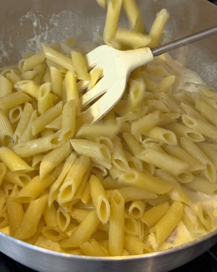 Ugotowany makaron penne dodawany na patelnię z kremowym sosem z boczkiem.