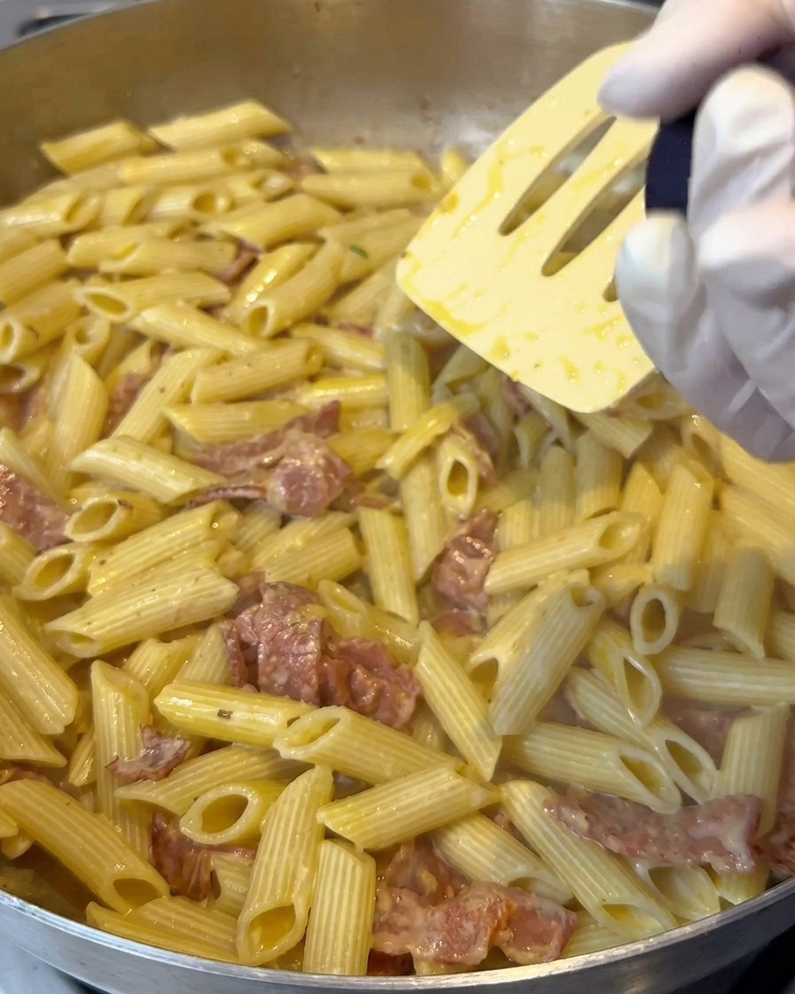 Sól cytrynowa mielona nad patelnią z kremowym makaronem penne podczas mieszania.
