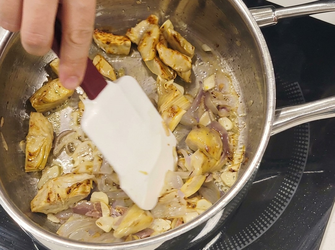 Podsmażone serca karczochów, plasterki czosnku i anchois smażące się razem na patelni ze stali nierdzewnej.