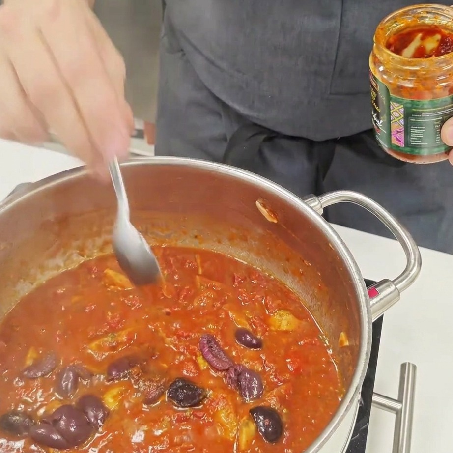 Łyżeczka sosu chili mieszana z gotującym się sosem pomidorowym do makaronu.