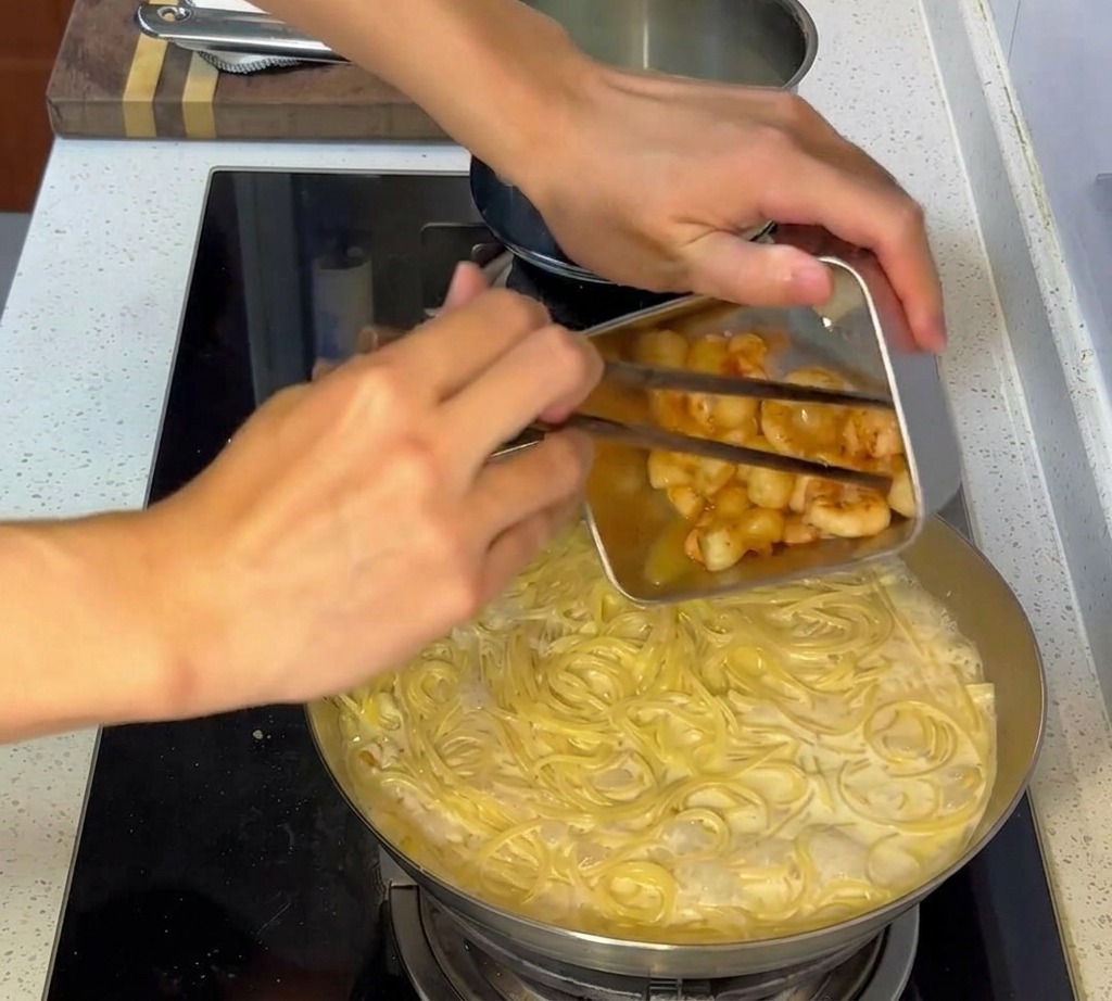 Podsmażone owoce morza dodawane na patelnię z wymieszanym kremowym makaronem.