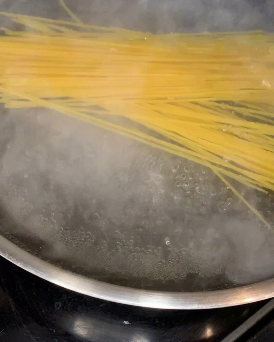 Nitki spaghetti mięknące w dużym garnku z gotującą się wodą.