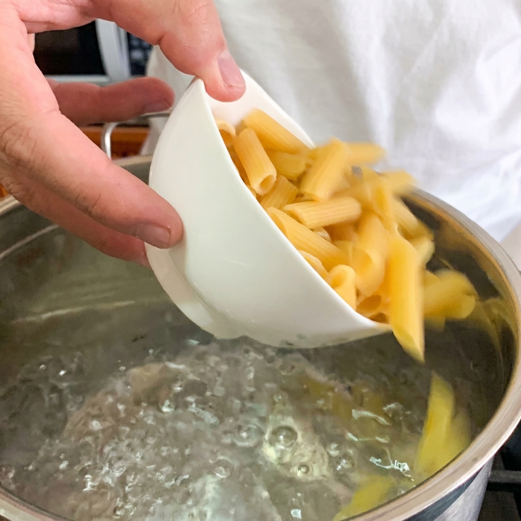Zbliżenie na układanie delikatnego jajka na środku miski z kremowym makaronem penne.
