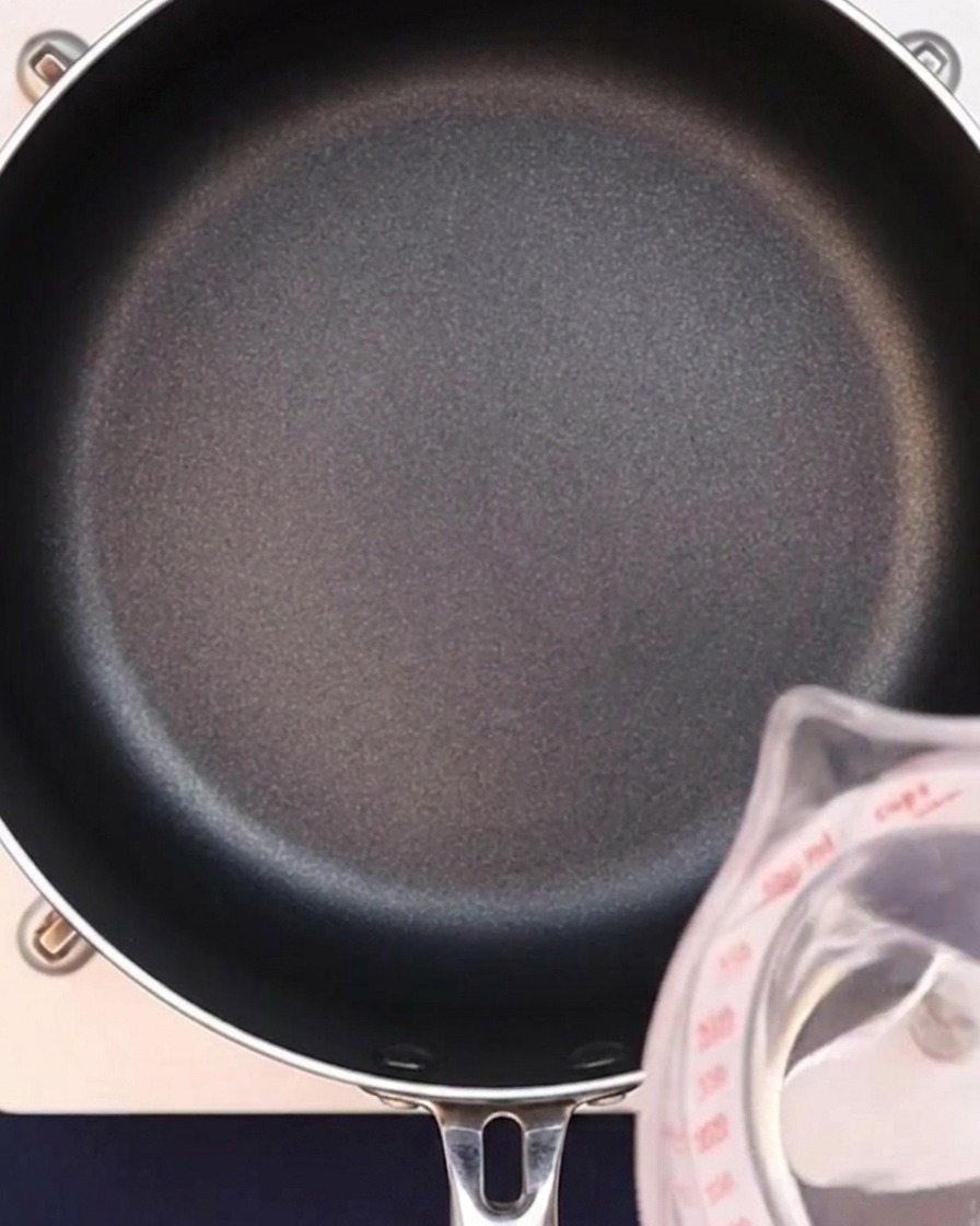 Woda wlewana do czarnego rondla w celu przygotowania bazy bulionu curry.