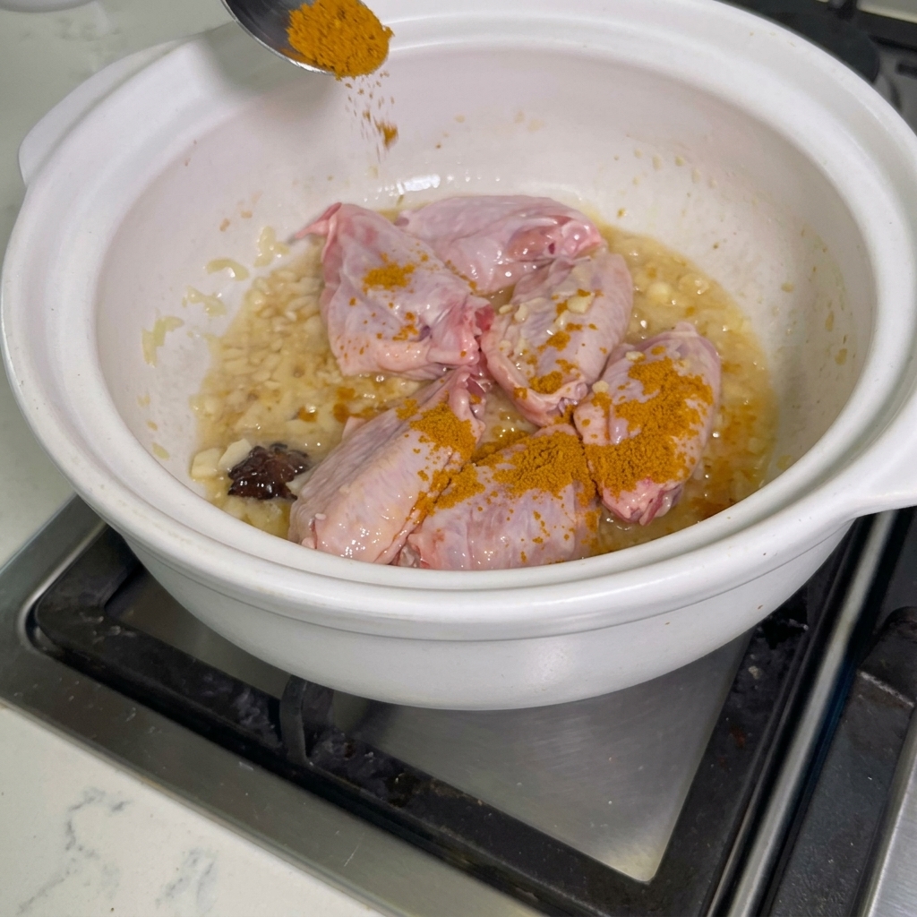 Przyprawa curry posypywana na skrzydełka z kurczaka w garnku.