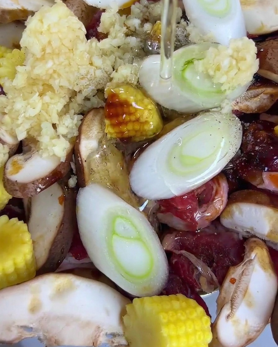 Olej wylewany na tacę z pokrojoną wołowiną, grzybami shiitake, mini kukurydzą, zieloną cebulką i czosnkiem.