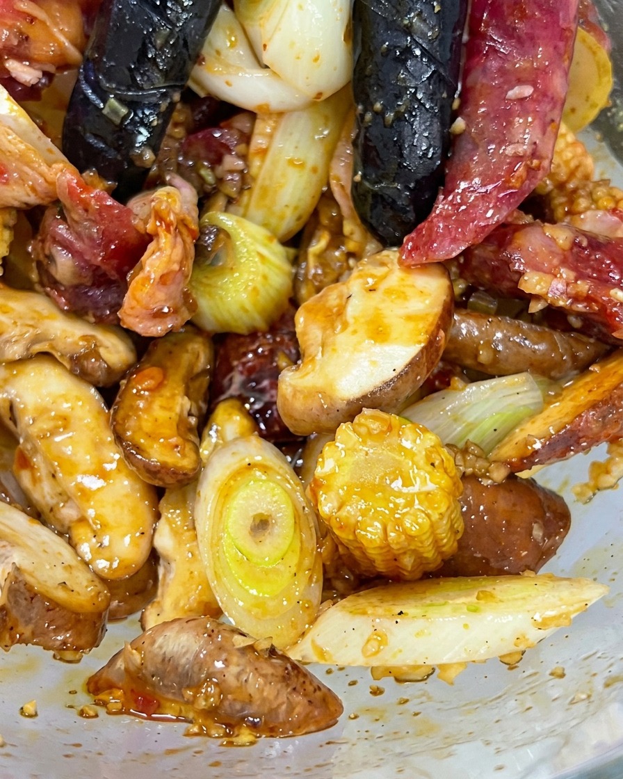 Dłonie w rękawiczkach mieszające wołowinę, grzyby, mini kukurydzę i aromaty w szklanej misce.