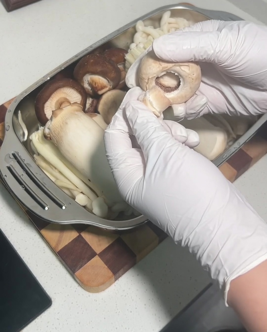 Dłoń usuwająca nóżkę z surowego kapelusza grzyba shiitake.