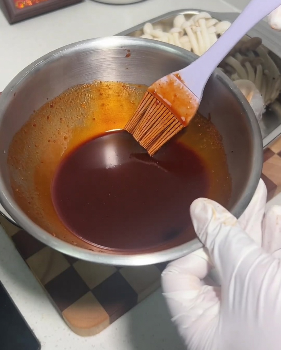 Metalowa miska z ciemną, pikantną mieszanką sosów mieszaną silikonowym pędzlem.