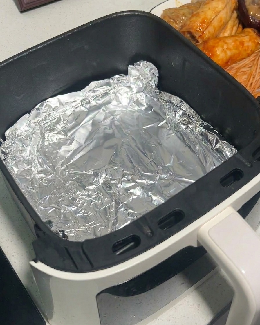Marynowane grzyby wkładane do koszyka frytkownicy wyłożonego folią aluminiową przy użyciu metalowych szczypiec.