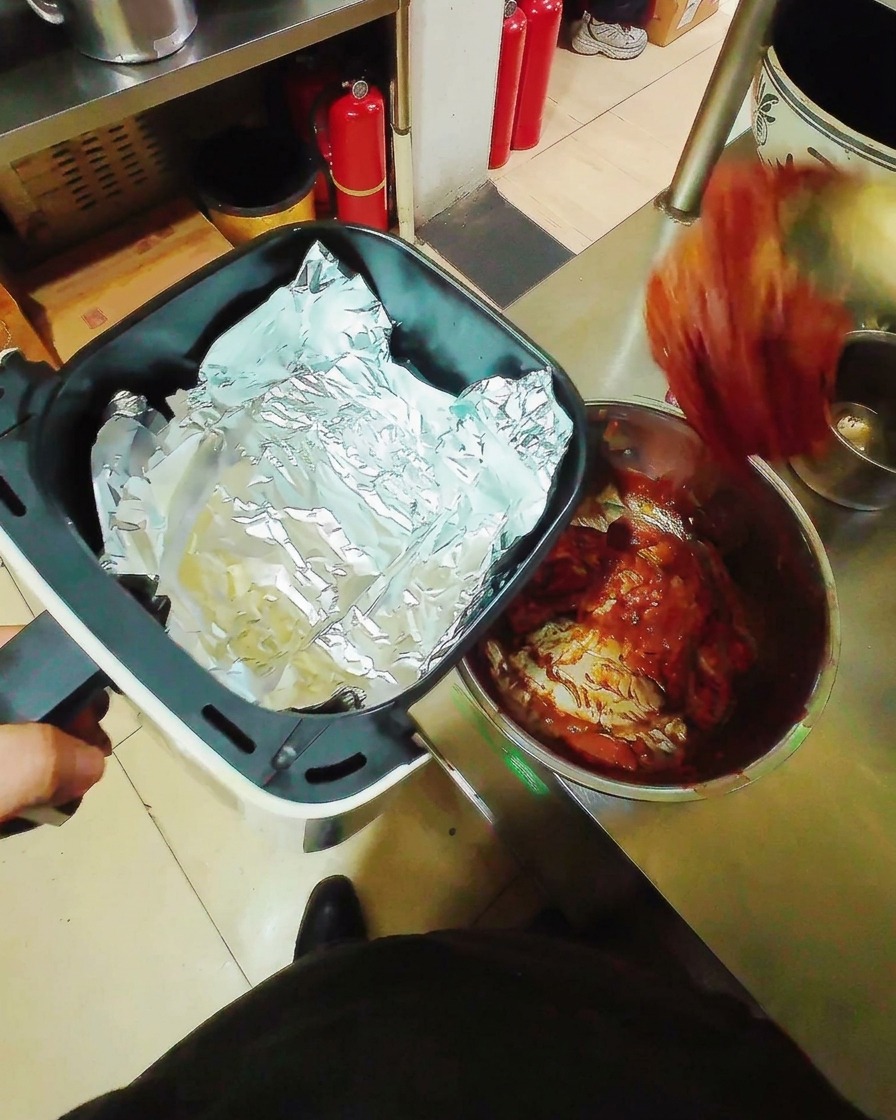 Zamarynowane paski boczku ułożone płasko na folii aluminiowej w koszu frytkownicy beztłuszczowej, gotowe do pieczenia.