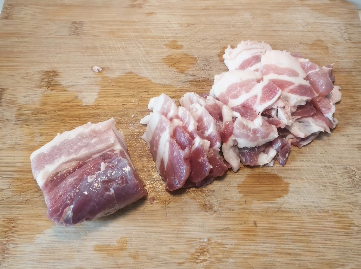 Cienkie, surowe plastry boczku równo ułożone na drewnianej desce po pokrojeniu.