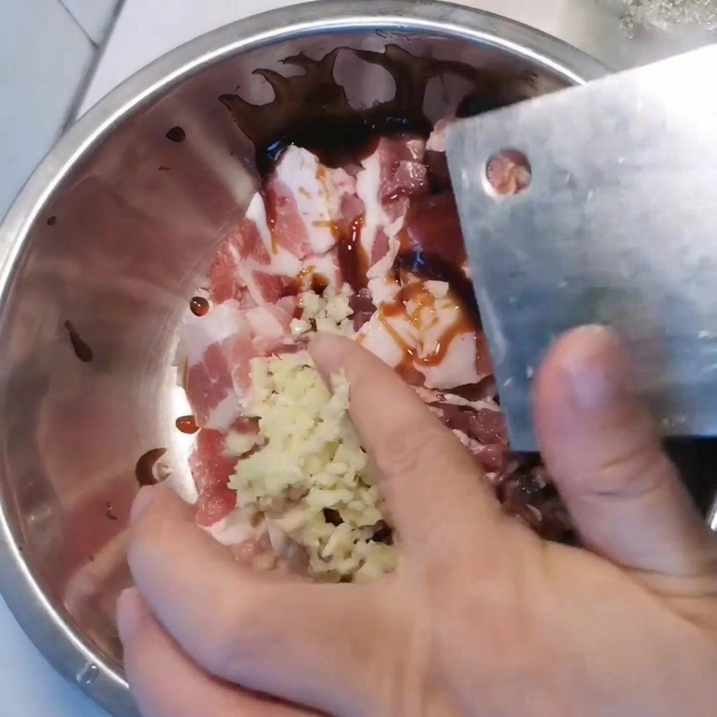 Metalowa miska z pokrojonym boczkiem, przyprawiana posiekanym czosnkiem i różnymi sosami.