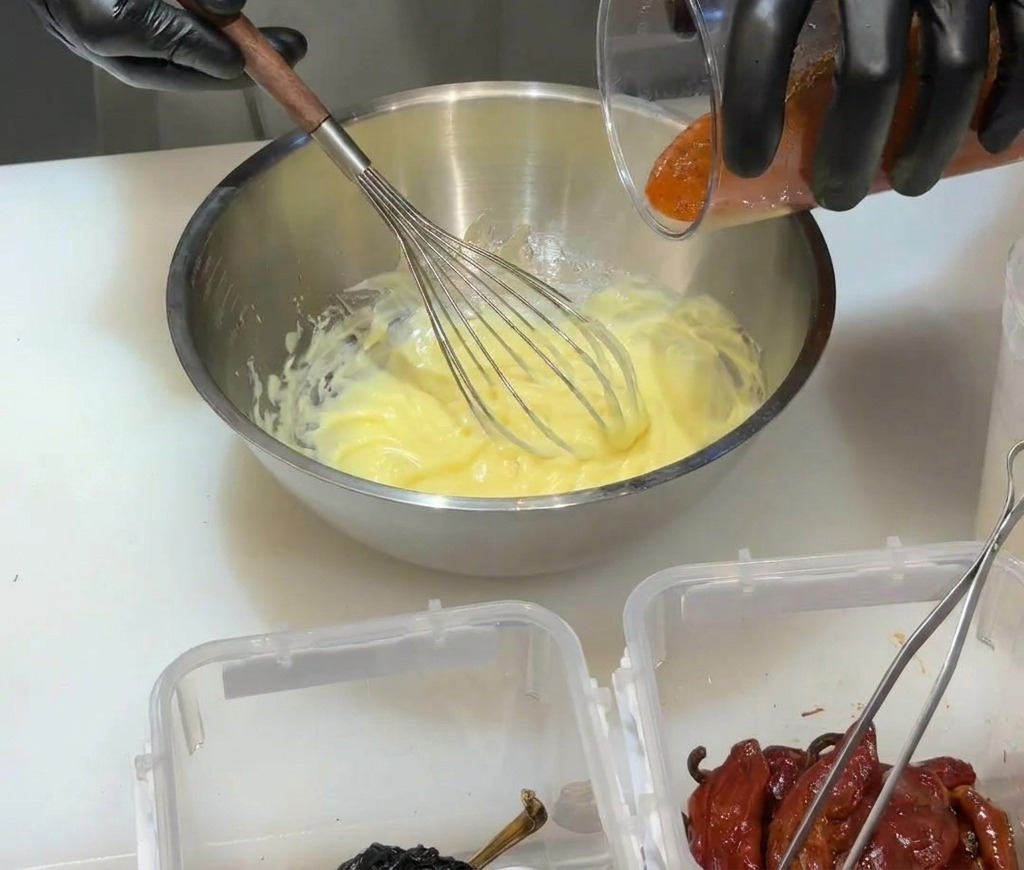 Wlewanie czerwonego, zblendowanego puree z chili do żółtej bazy majonezowej w metalowej misce.