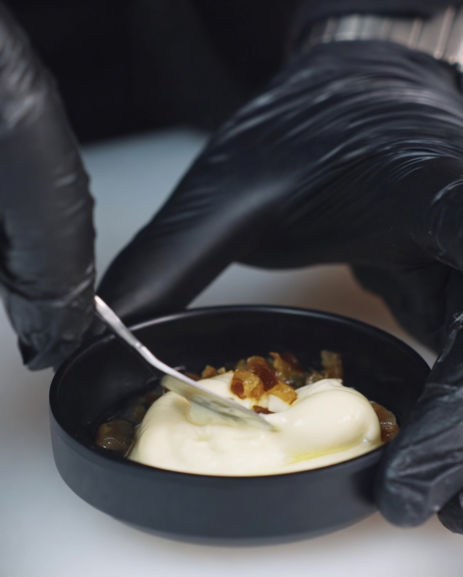 Zbliżenie na małą miseczkę z majonezem, posiekanymi meksykańskimi papryczkami chili i wodą po ogórkach kiszonych, wymieszanymi metalową łyżką.
