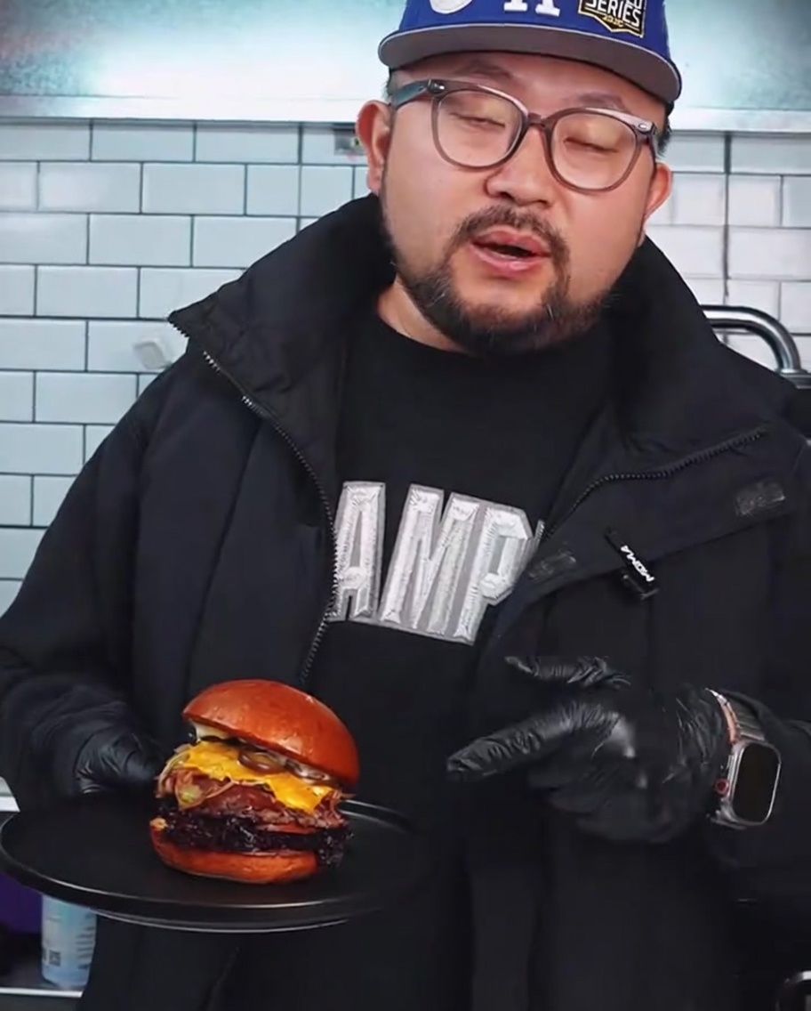 Surowy kotlet z wołowiny Wagyu spłaszczany na gorącym grillu za pomocą ciężkiej metalowej prasy do burgerów.