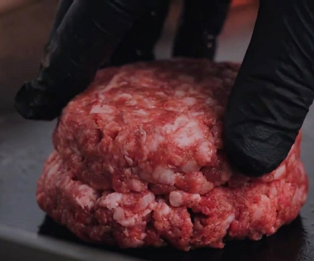 Surowy kotlet z wołowiny Angus dociskany do gorącego grilla.