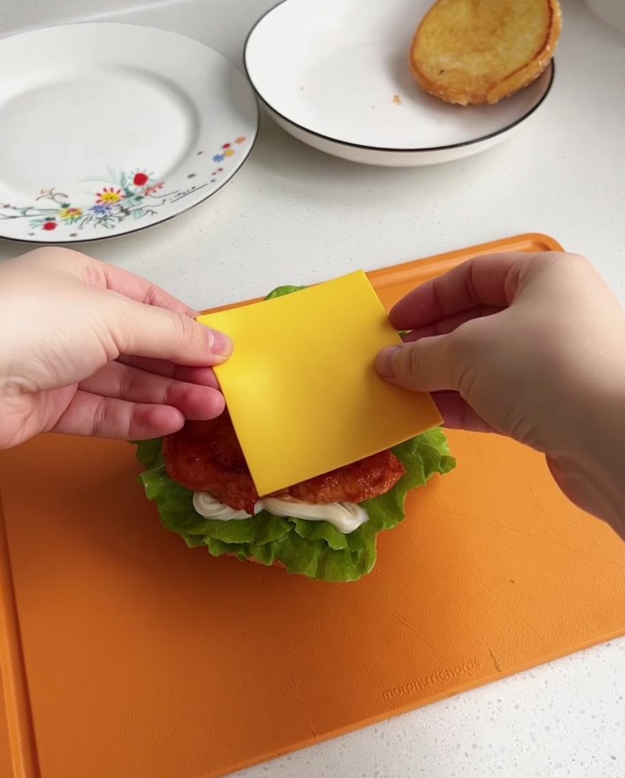 Plaster żółtego sera układany na gorącym kurczaku na burgerze.
