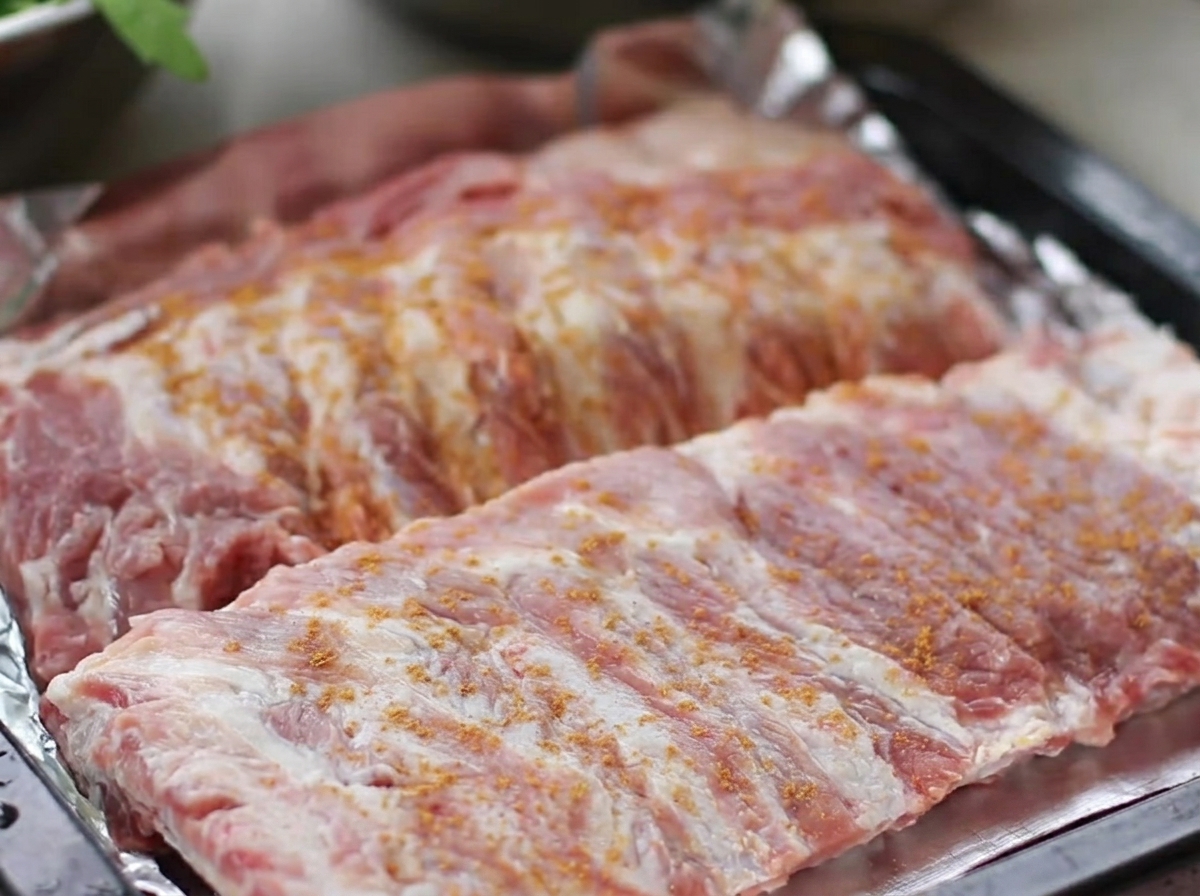 Surowe żeberka wieprzowe ułożone na blasze do pieczenia, obficie natarte mieszanką przyprawy pięciu smaków, czarnego pieprzu, imbiru i czosnku.