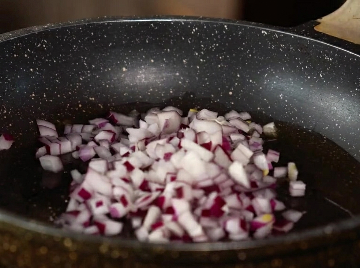 Pokrojona cebula, czosnek i imbir smażące się na patelni z olejem.