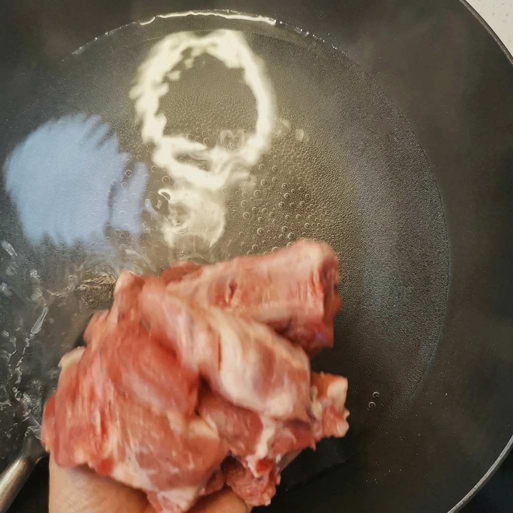 Żeberka wieprzowe blanszowane w garnku z wrzącą wodą i winem do gotowania, widoczna piana na powierzchni.