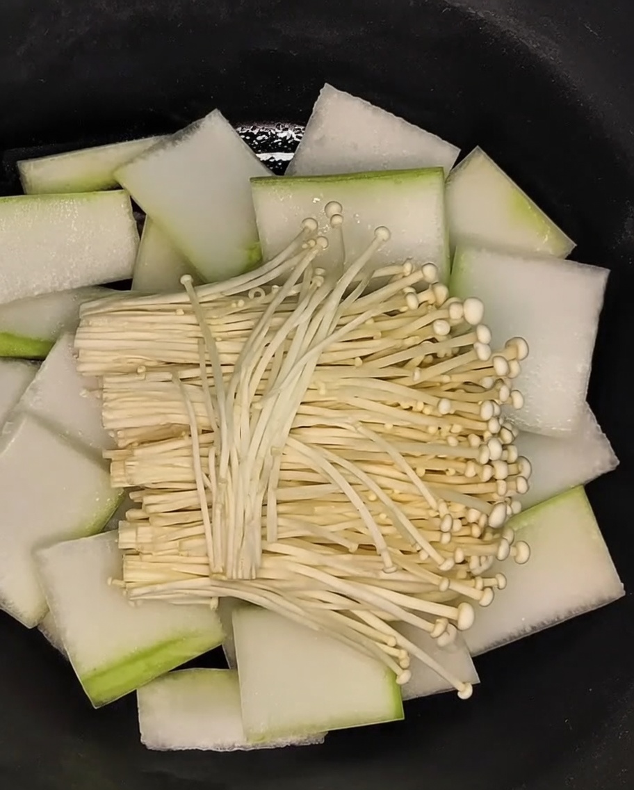 Pęczek grzybów enoki układany na warstwie melona zimowego.