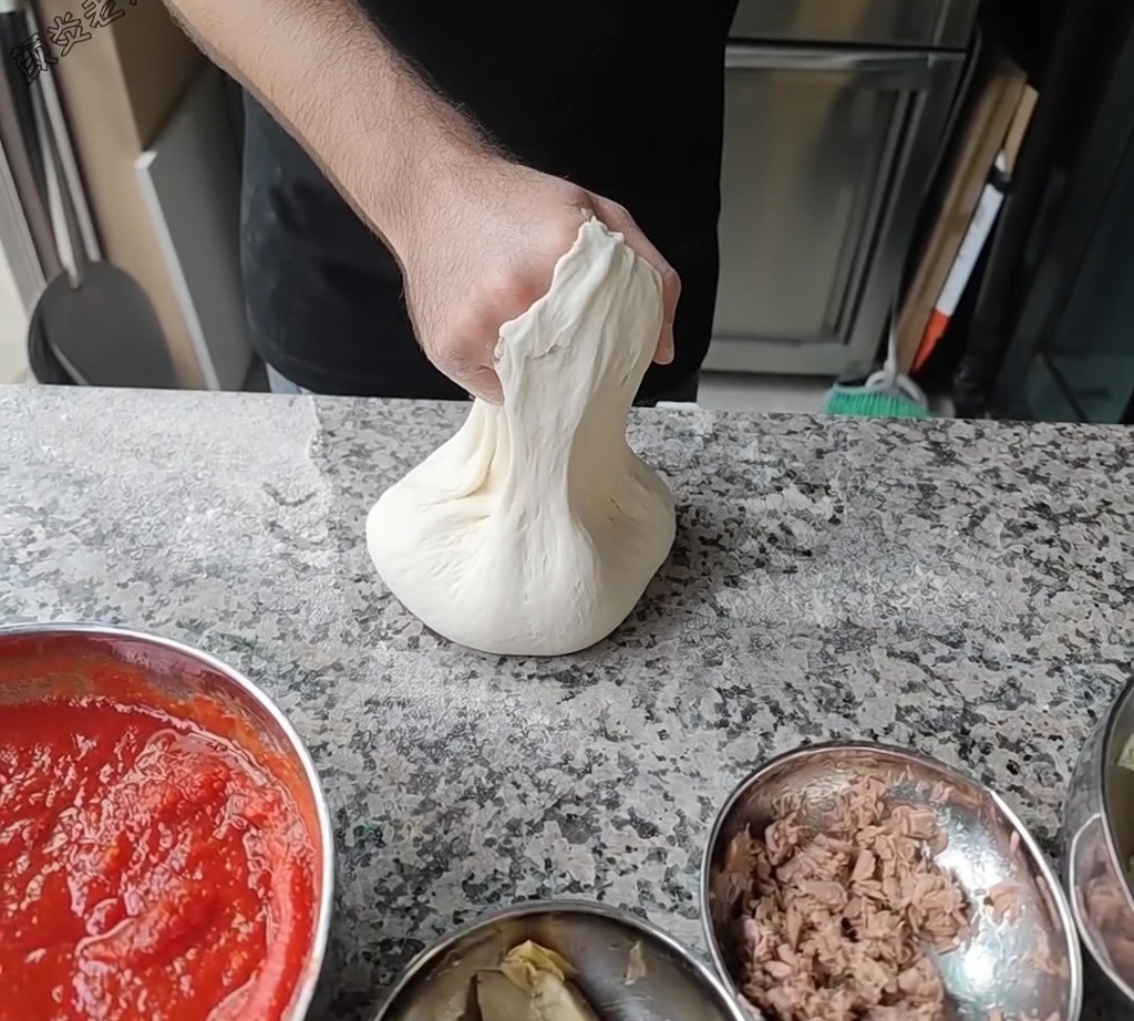 Szef kuchni rozciągający ciasto na pizzę, obracając je na knykciach, aby uzyskać pożądaną średnicę.