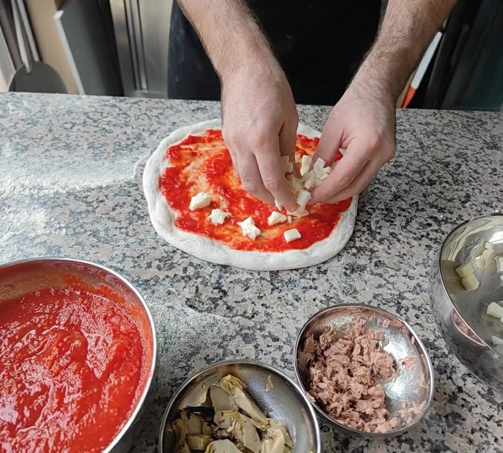 Małe kostki świeżego białego sera mozzarella rozsypywane na bazie z sosem pomidorowym.