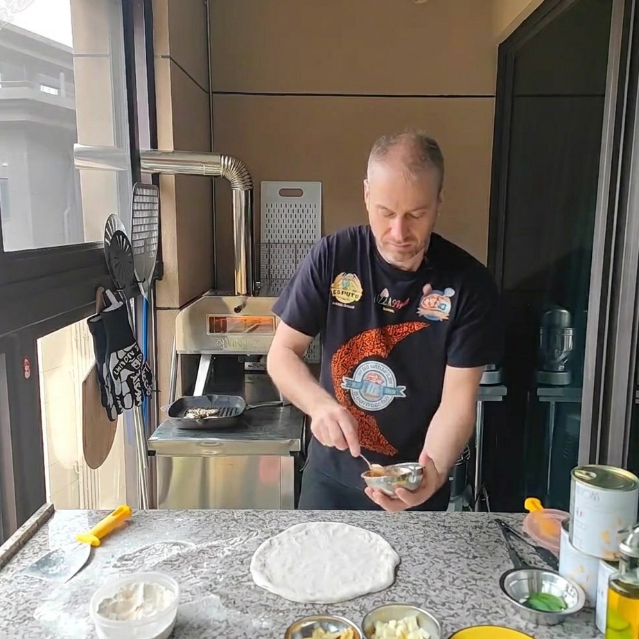 Łyżka rozprowadzająca jasnoczerwony sos pomidorowy na okrągłym spodzie do pizzy.