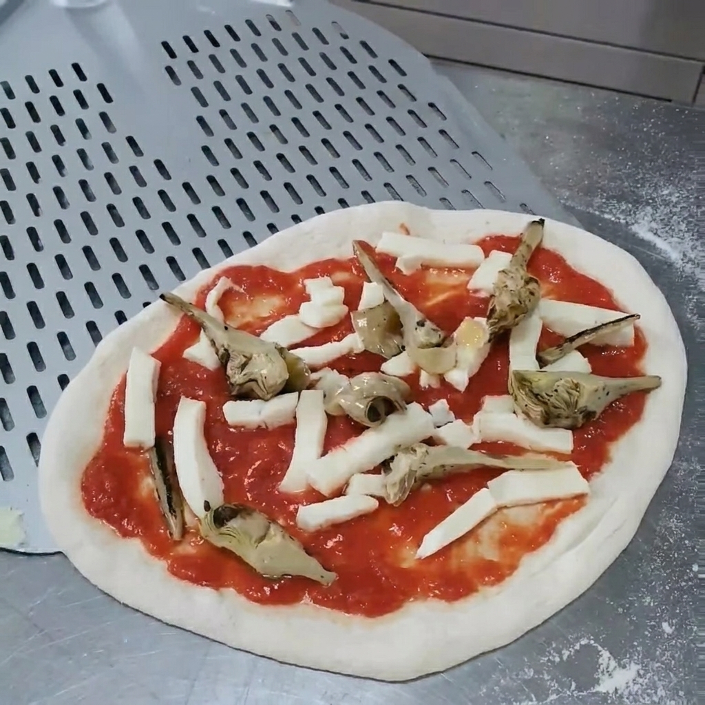 Ręce poprawiające położenie grillowanych karczochów na surowej pizzy, aby zapewnić równomierne rozmieszczenie.