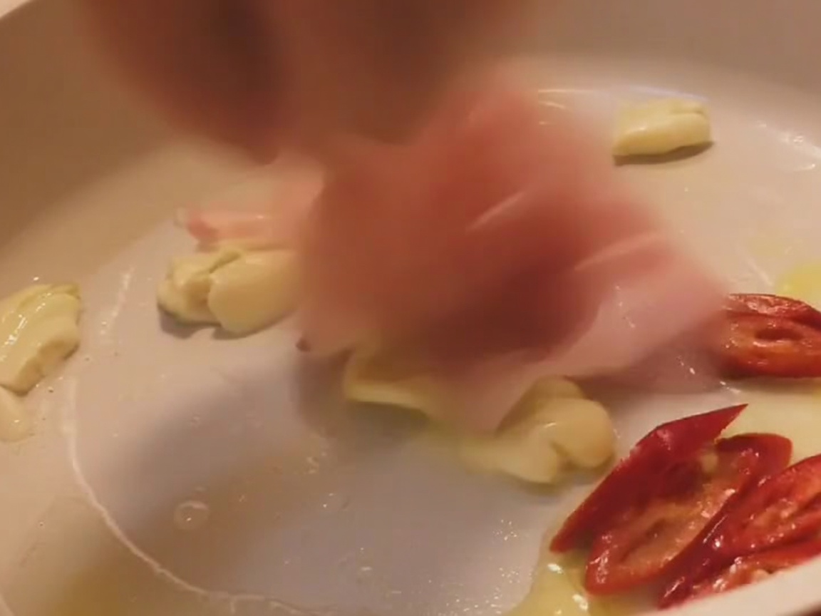Paski boczku smażące się na jasnej patelni z czosnkiem i plasterkami czerwonego chili.