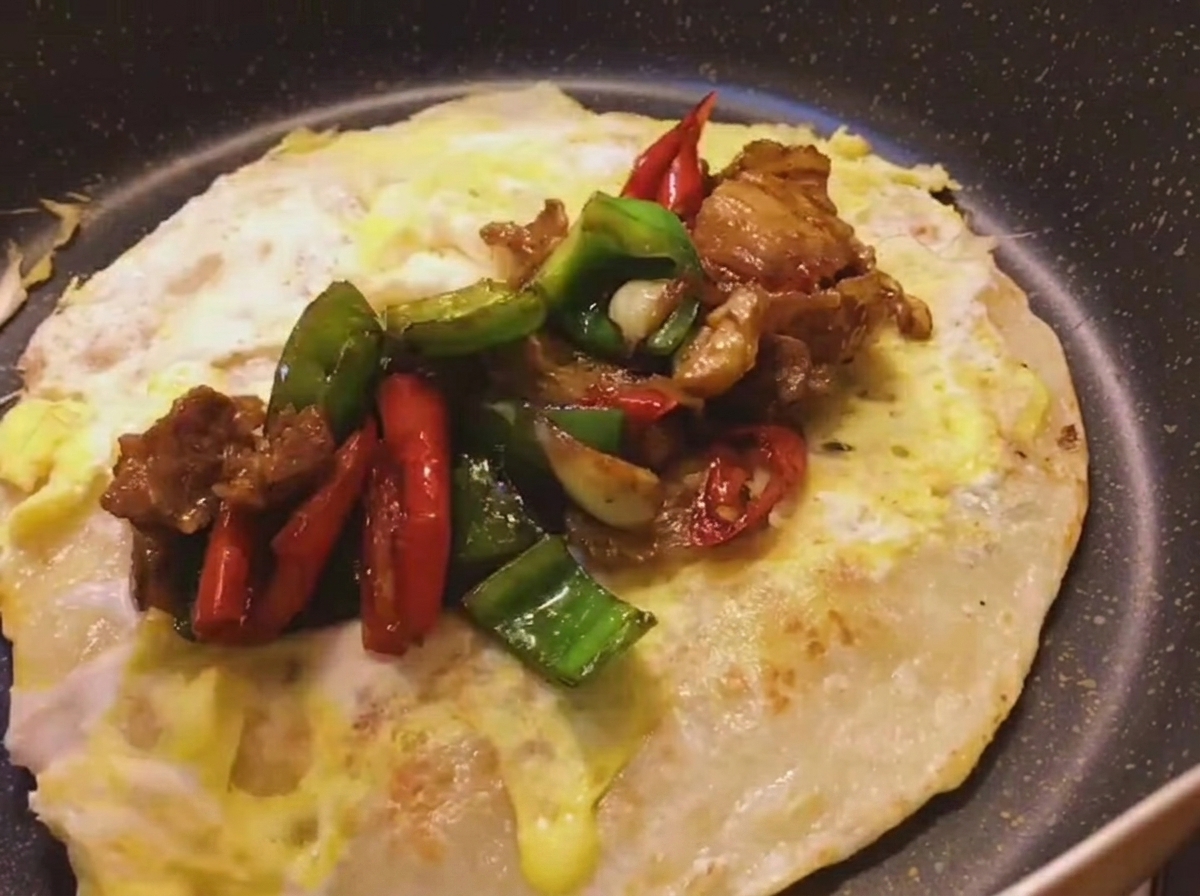 Pikantny stir-fry z boczku i papryki nakładany na środek złocistego placka z usmażonym jajkiem.