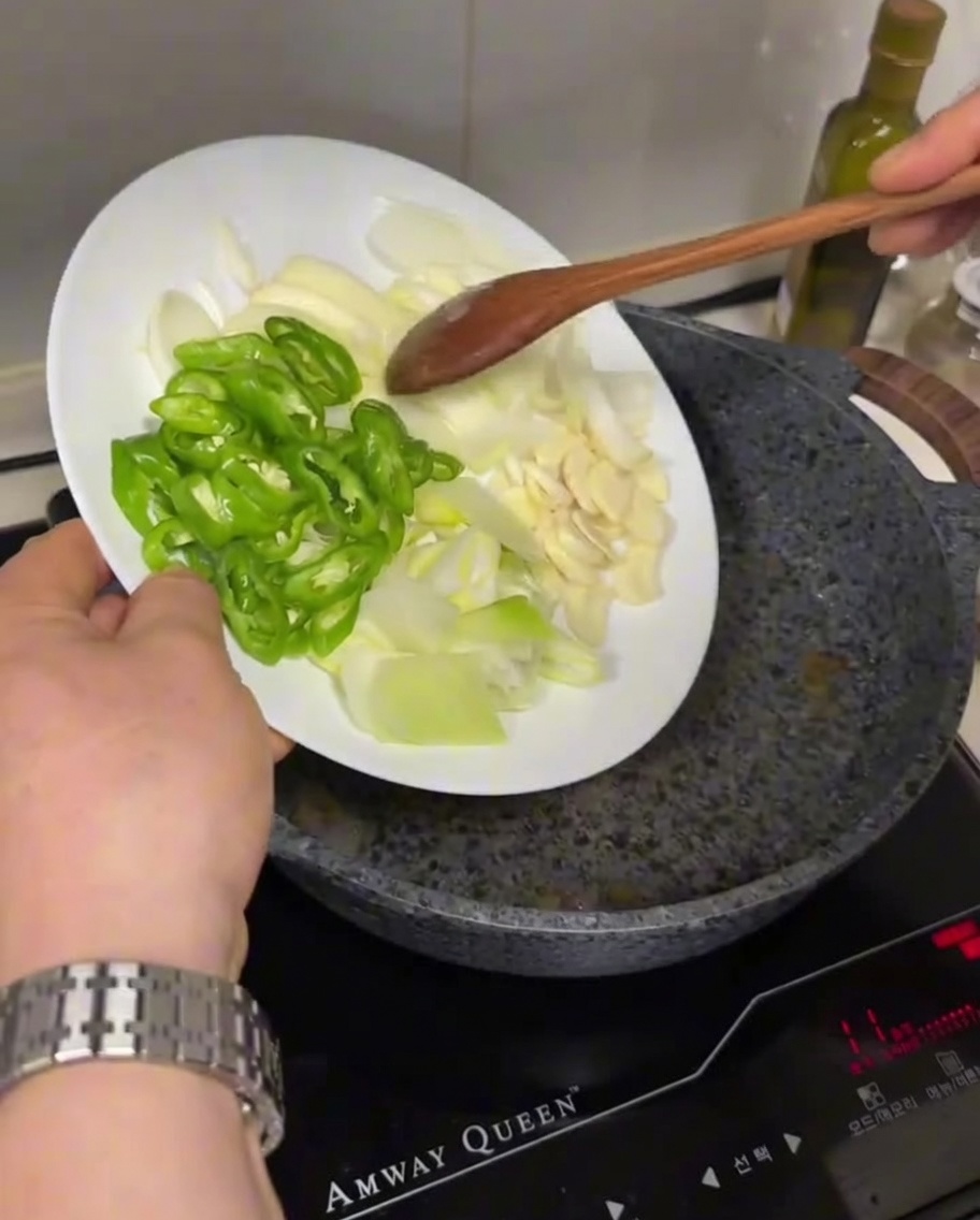 Pokrojone zielone chili, cebula i czosnek dodawane do gorącej, naoliwionej patelni.