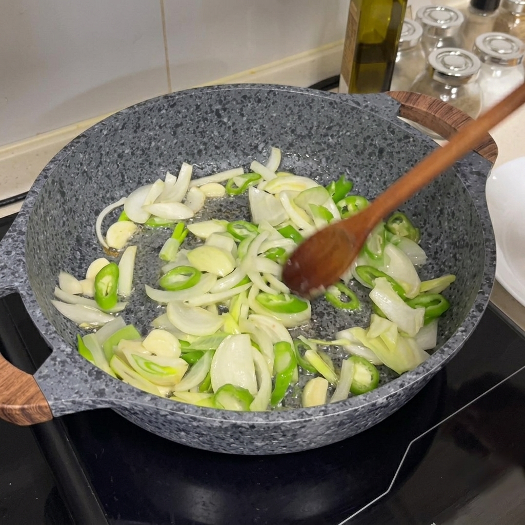 Cebula, chili i czosnek smażone na gorącej patelni za pomocą drewnianej łyżki.