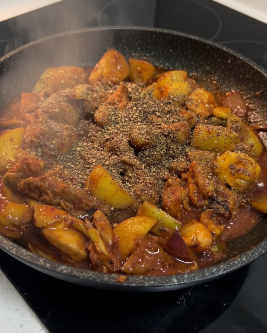 Pikantny koreański kurczak posypywany sproszkowaną pachnotką na patelni.