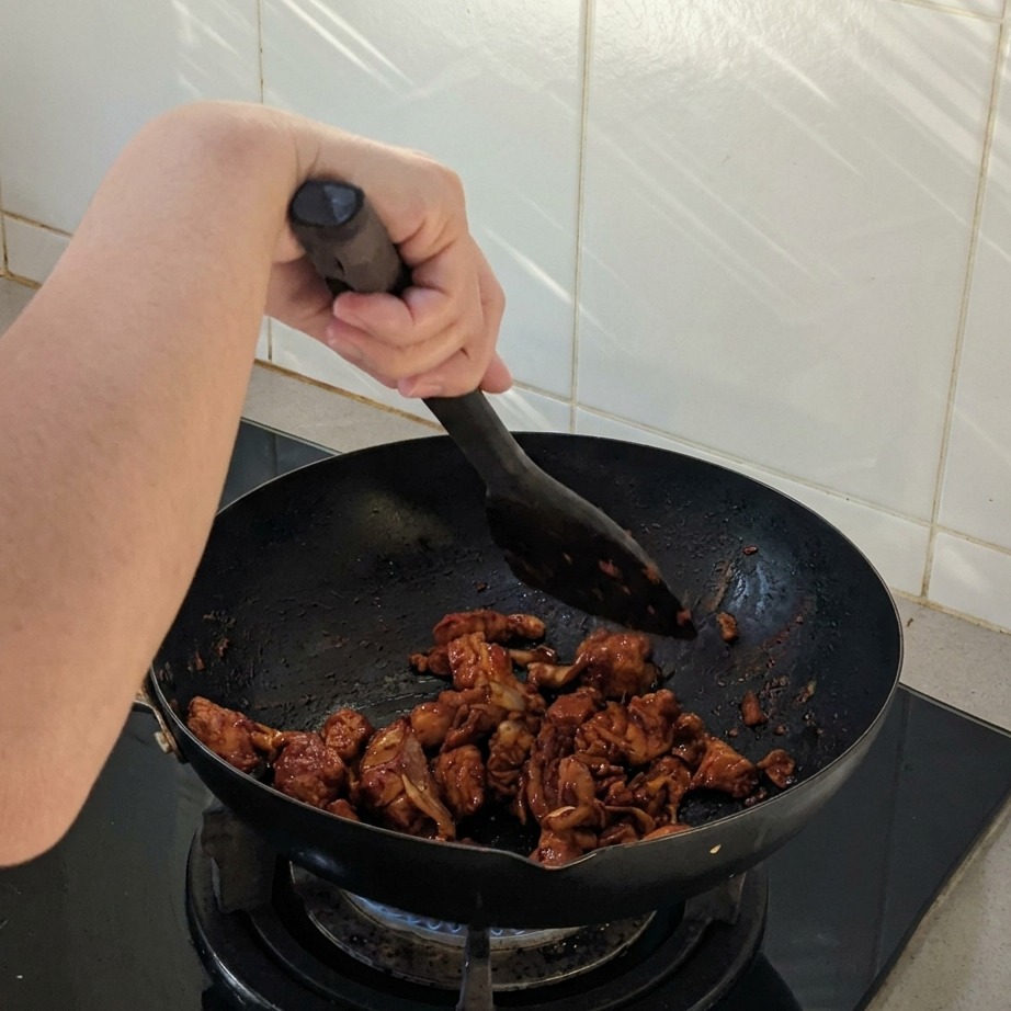 Kawałki kurczaka i cebuli smażone w czarnym woku łopatką, pokryte ciemnym, pikantnym sosem.
