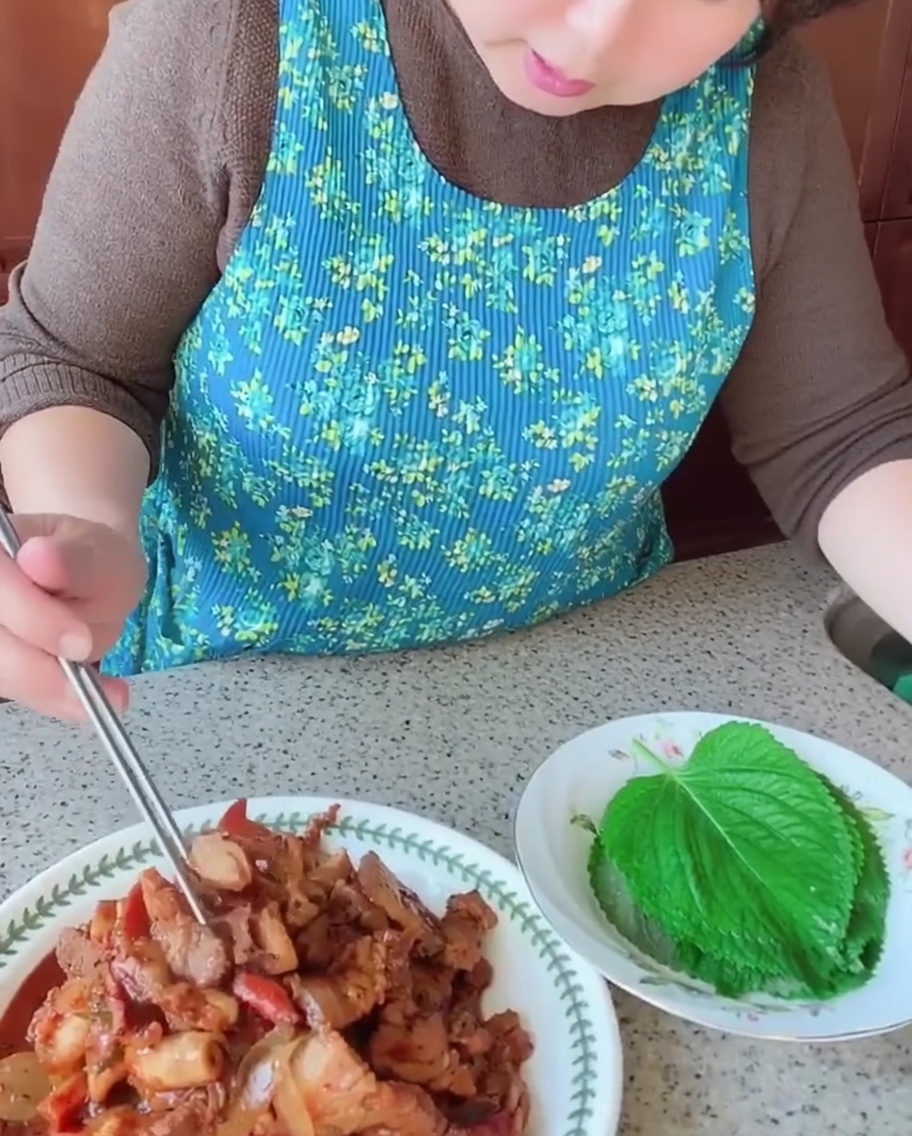 Osoba używająca pałeczek, aby położyć kawałek usmażonego boczku i kalmara na świeżym, zielonym liściu pachnotki.