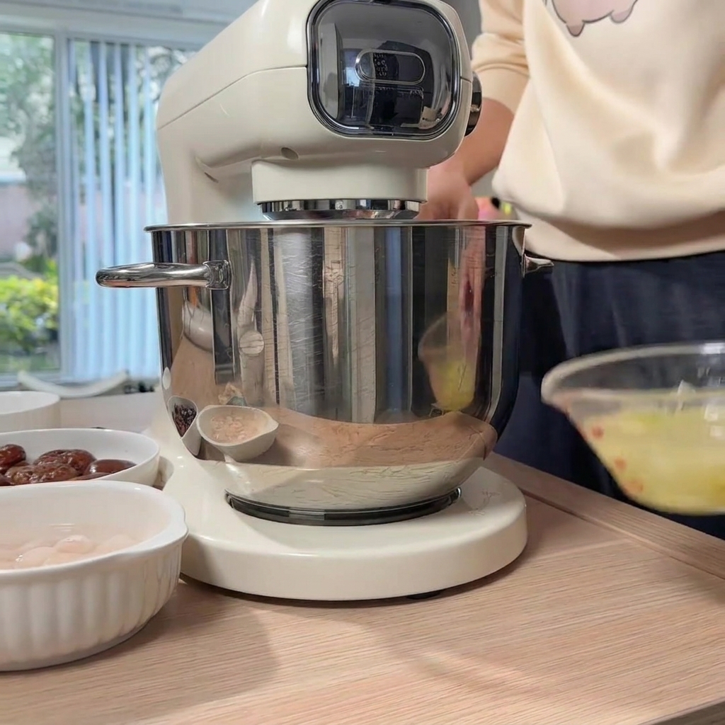 Ręka wlewająca przygotowaną wodę z imbirem i szczypiorkiem ze szklanej miski do miski robota kuchennego z mielonym kurczakiem.