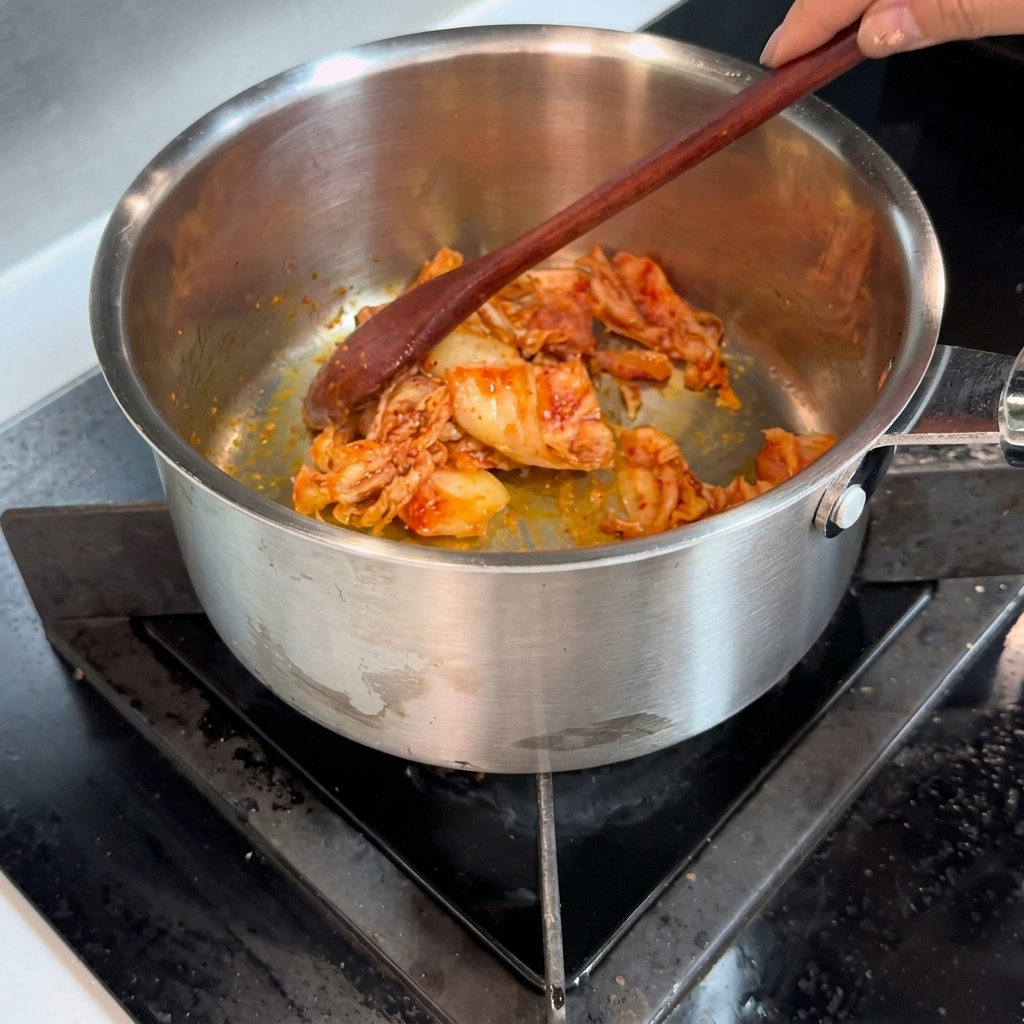 Drewniana łyżka mieszająca jasnoczerwone posiekane kimchi w stalowym garnku.