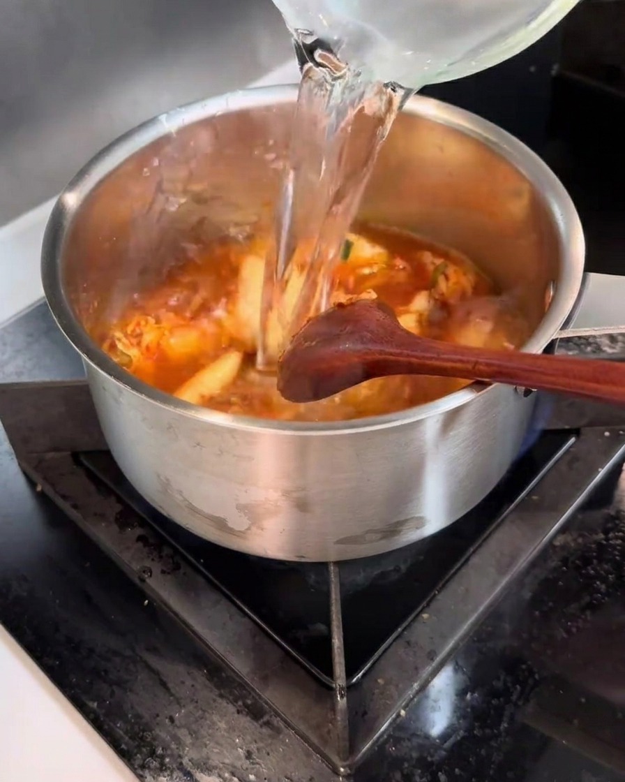 Woda wlewana z dzbanka do garnka z pikantną mieszanką kimchi.