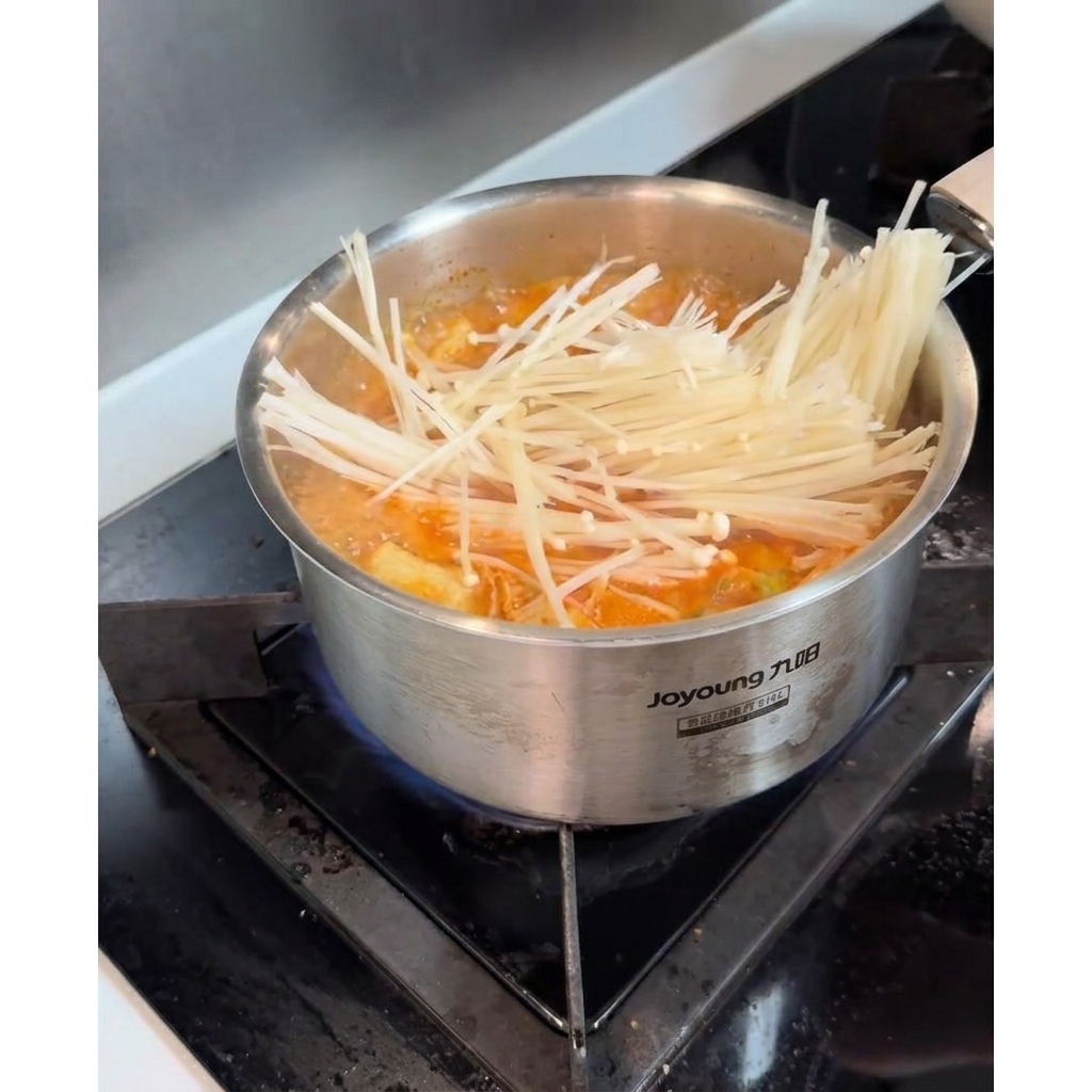Świeże grzyby enoki wrzucane do bulgoczącej zupy kimchi.
